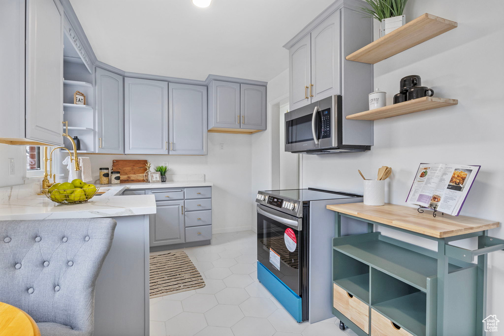 Kitchen with light tile patterned flooring, stainless steel appliances, sink, and gray cabinetry