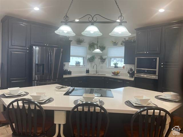 Kitchen featuring pendant lighting, sink, a center island, black electric stovetop, and stainless steel fridge with ice dispenser