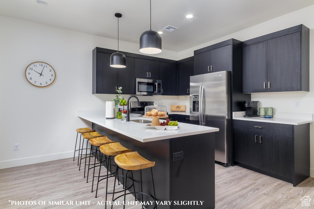 Kitchen with a breakfast bar area, hanging light fixtures, light hardwood / wood-style flooring, appliances with stainless steel finishes, and kitchen peninsula