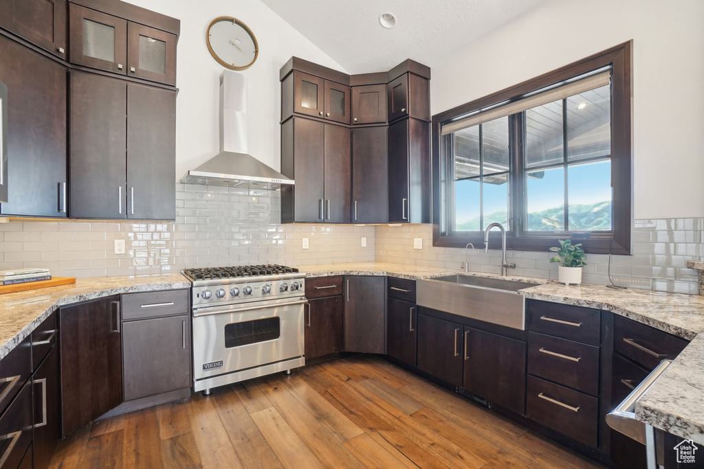 Kitchen with luxury range, wall chimney exhaust hood, lofted ceiling, dark wood-type flooring, and a sink
