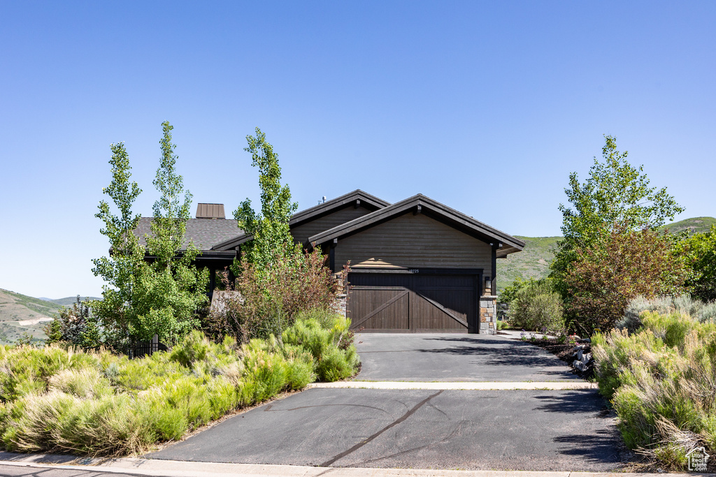 View of front of property with driveway, an attached garage, stone siding, and a mountain view