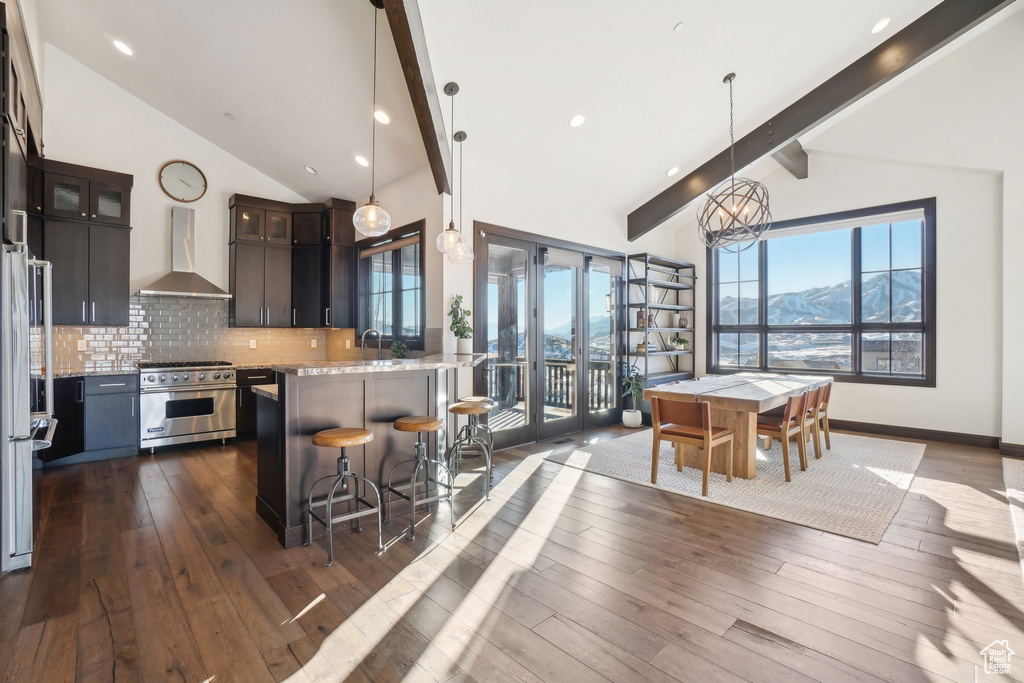 Kitchen featuring luxury stove, wall chimney range hood, beamed ceiling, backsplash, and a kitchen breakfast bar