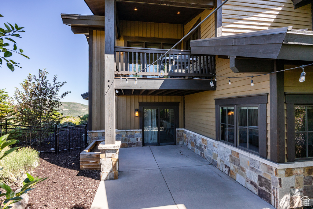 Back of property with a balcony, stone siding, a mountain view, and a patio area