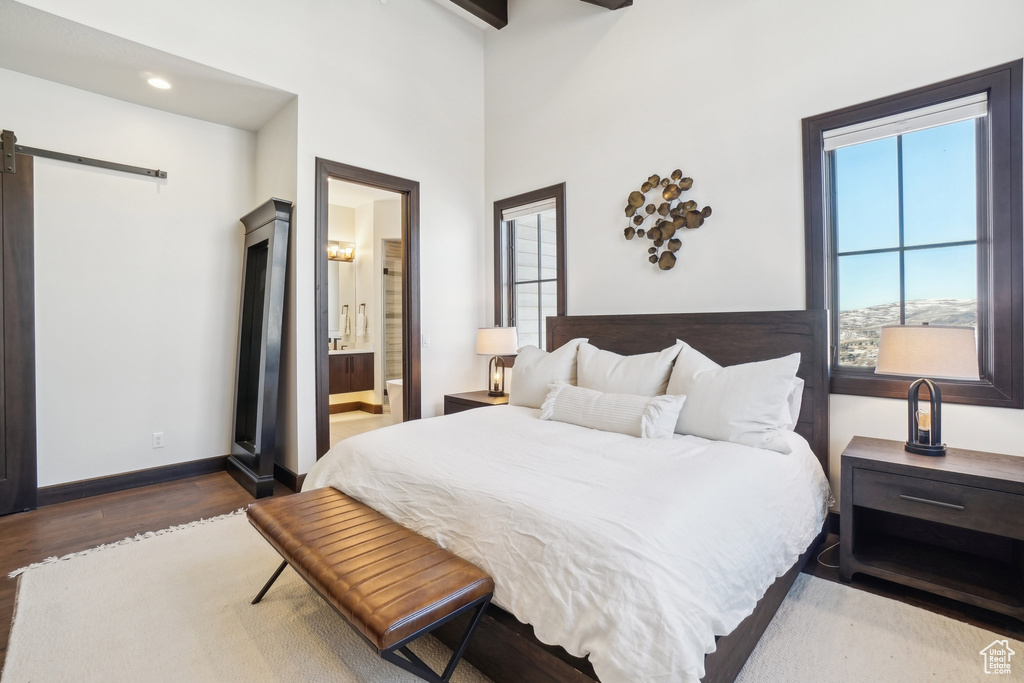 Bedroom with a barn door, wood finished floors, baseboards, connected bathroom, and recessed lighting
