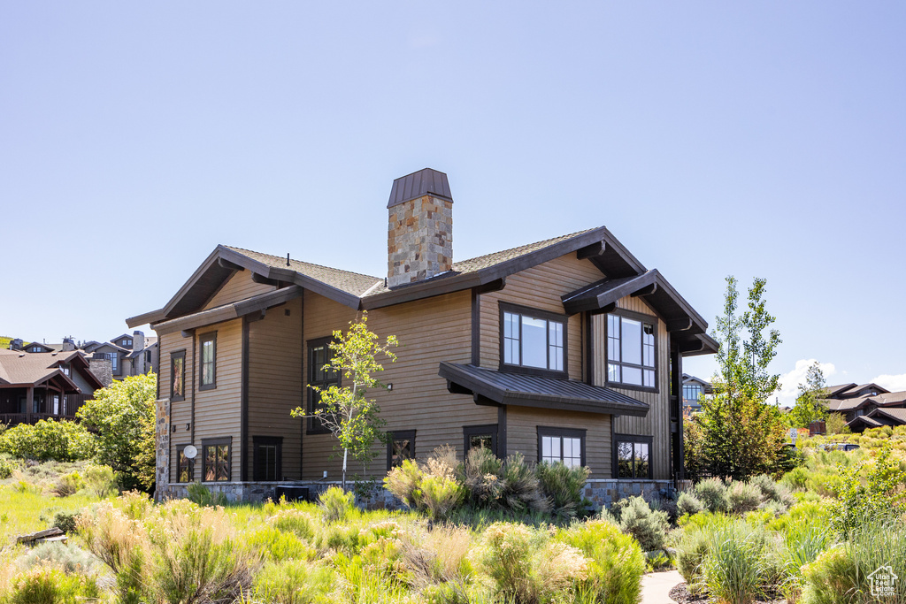 Back of property featuring a chimney, metal roof, a standing seam roof, and stone siding