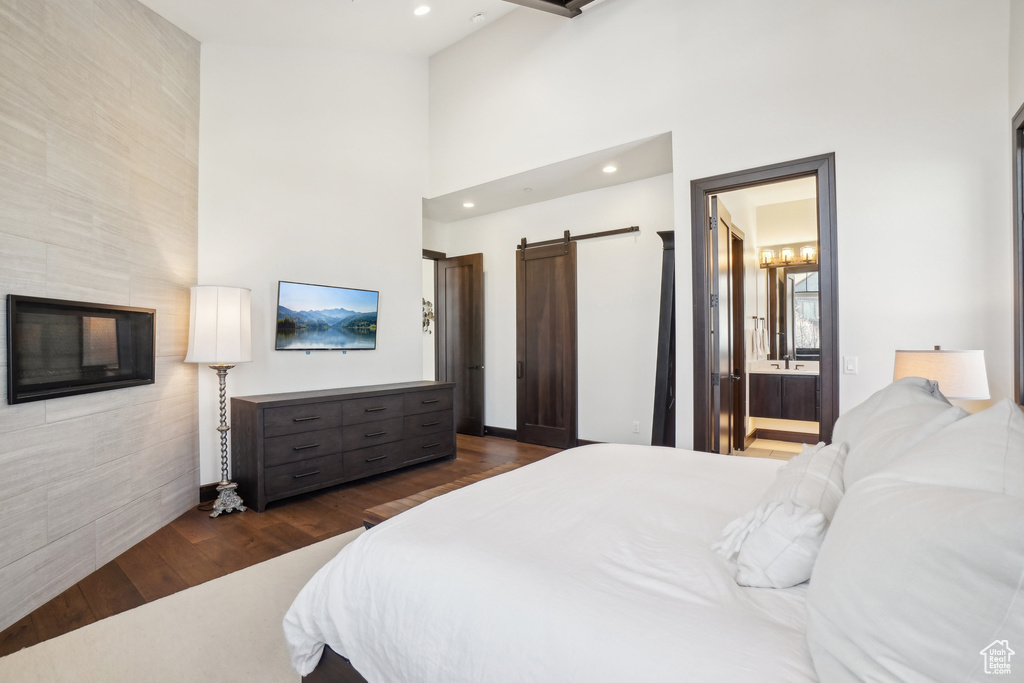 Bedroom with a barn door, dark wood-style flooring, recessed lighting, a towering ceiling, and ensuite bath