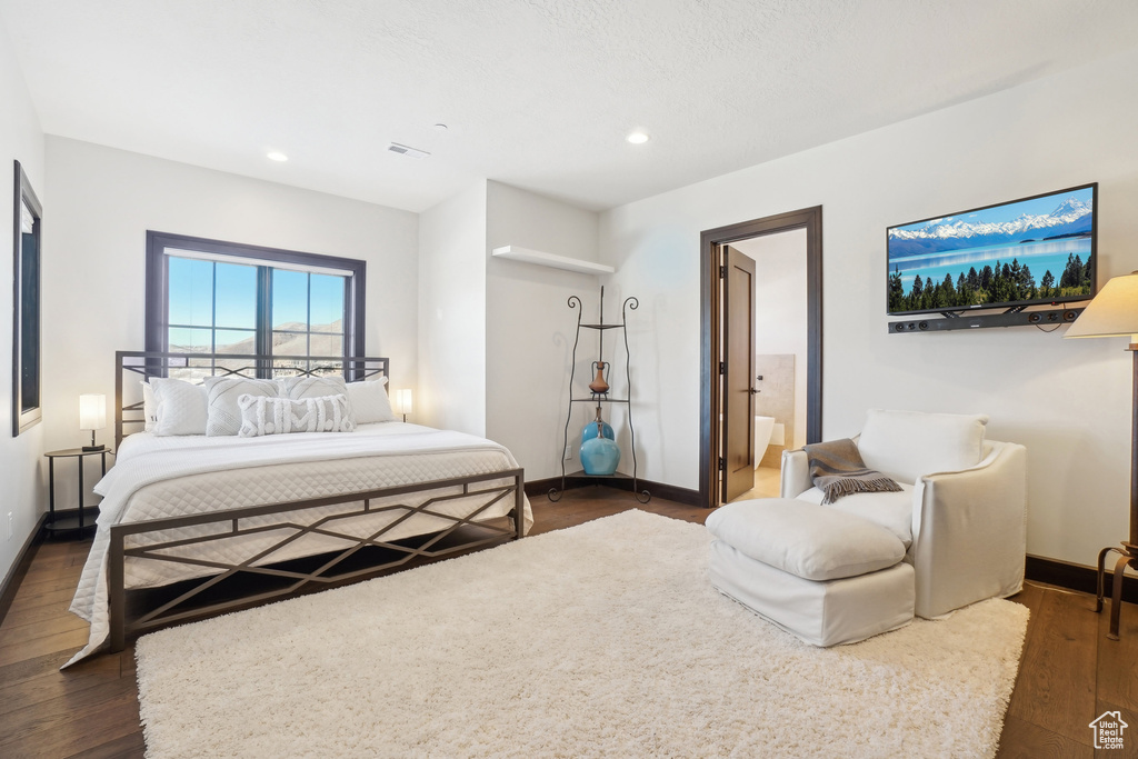 Bedroom with dark wood finished floors, baseboards, recessed lighting, and connected bathroom