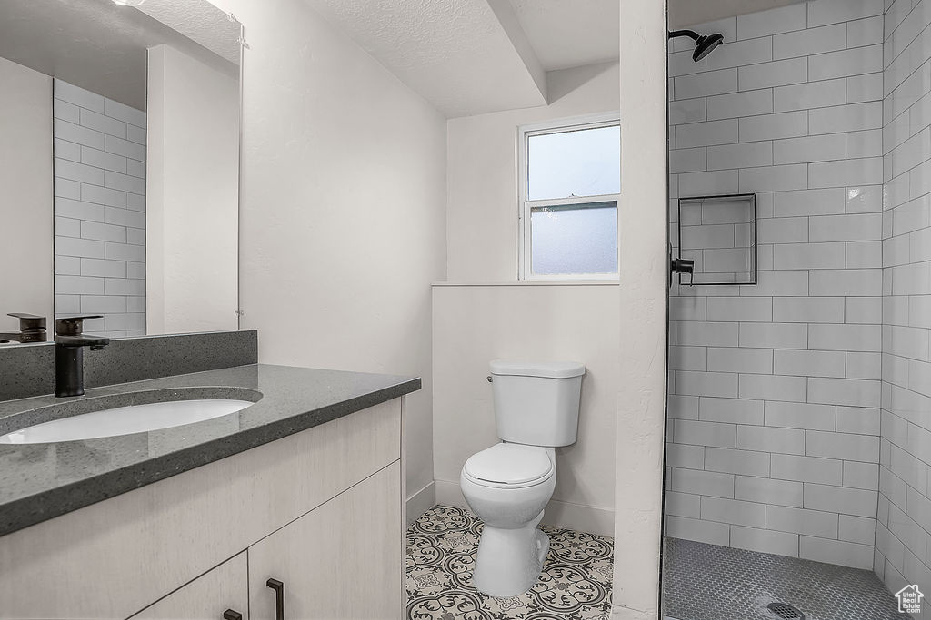 Bathroom featuring tile patterned flooring, vanity, a tile shower, a textured ceiling, and toilet