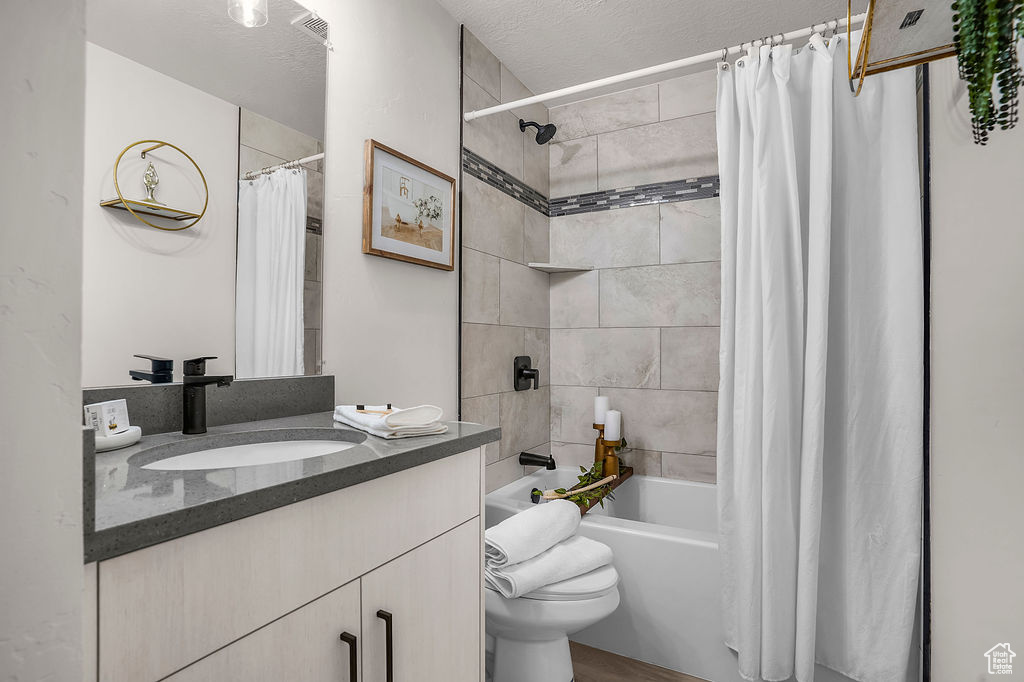 Full bathroom with shower / bathtub combination with curtain, vanity, a textured ceiling, and toilet