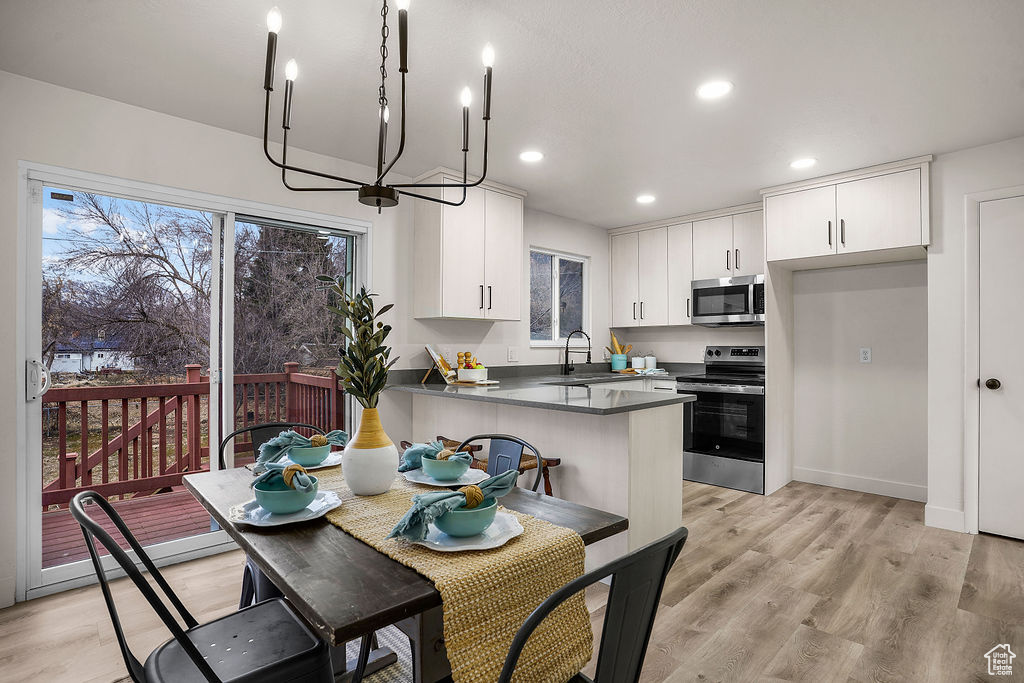 Kitchen featuring sink, appliances with stainless steel finishes, kitchen peninsula, light hardwood / wood-style floors, and white cabinets