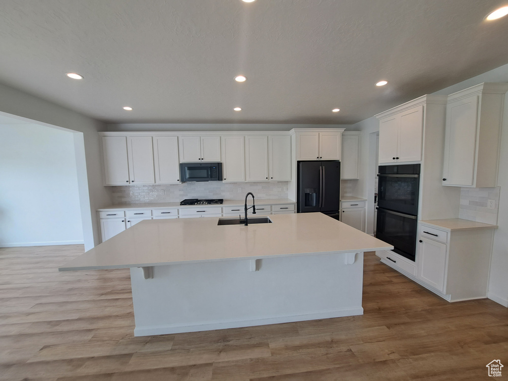 Kitchen featuring a sink, black appliances, tasteful backsplash, a center island with sink, and recessed lighting