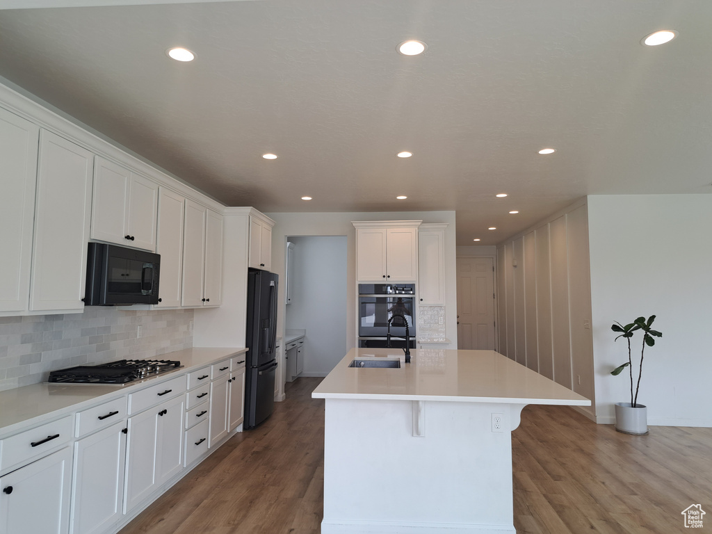 Kitchen featuring black appliances, a sink, white cabinetry, a center island with sink, and decorative backsplash