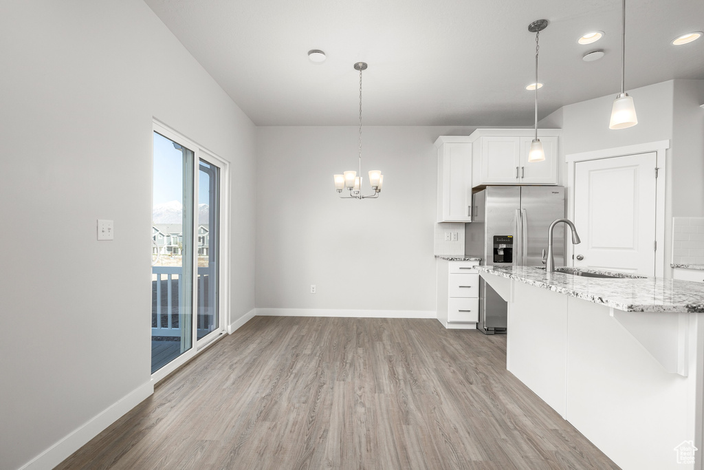 Kitchen featuring pendant lighting, white cabinets, light hardwood / wood-style floors, stainless steel fridge with ice dispenser, and light stone countertops