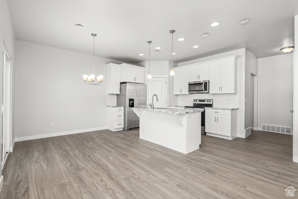 Kitchen featuring pendant lighting, an island with sink, white cabinets, stainless steel appliances, and light wood-type flooring