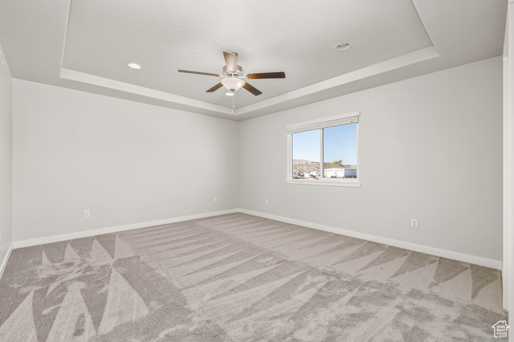 Carpeted spare room with a tray ceiling and ceiling fan