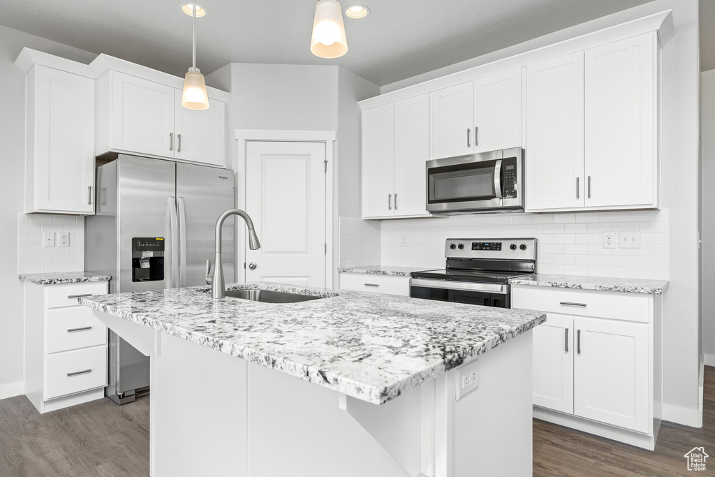 Kitchen with sink, appliances with stainless steel finishes, pendant lighting, a kitchen island with sink, and white cabinets