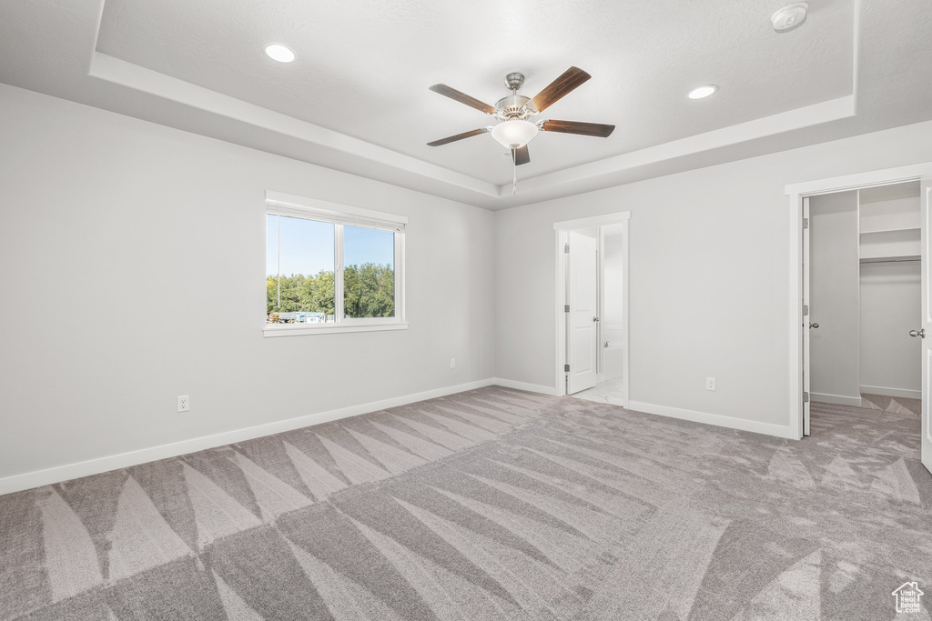 Unfurnished bedroom featuring a spacious closet, light colored carpet, ceiling fan, and a tray ceiling