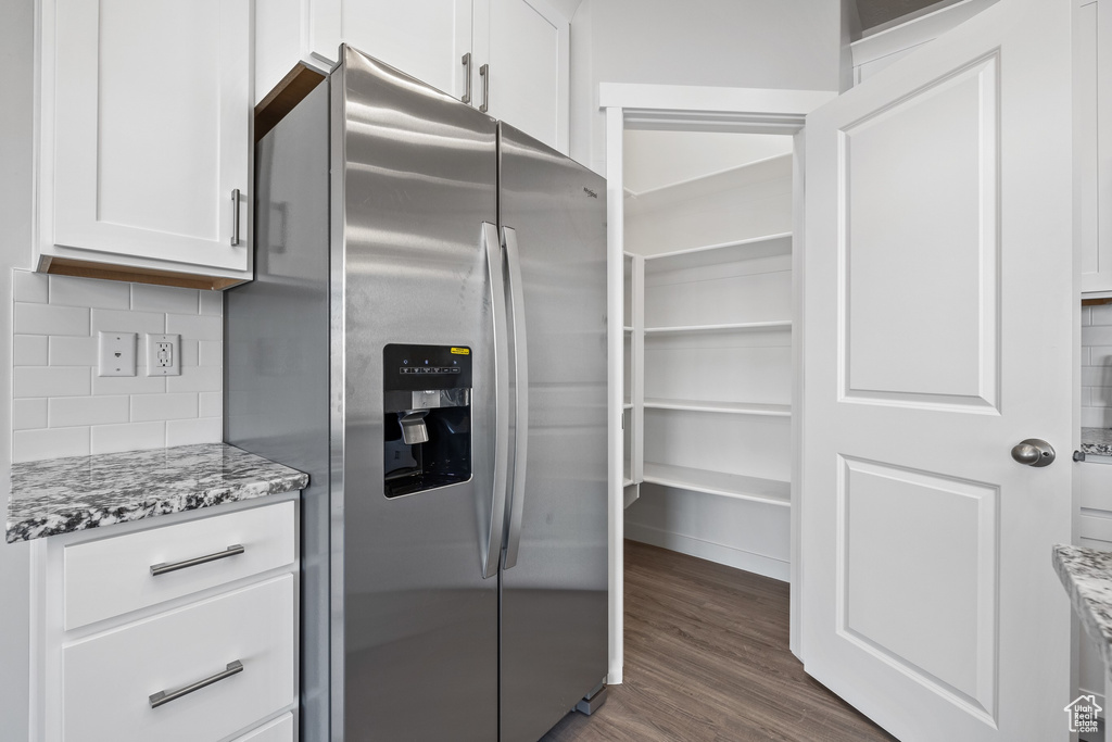 Kitchen featuring white cabinets, light stone countertops, stainless steel fridge, and backsplash