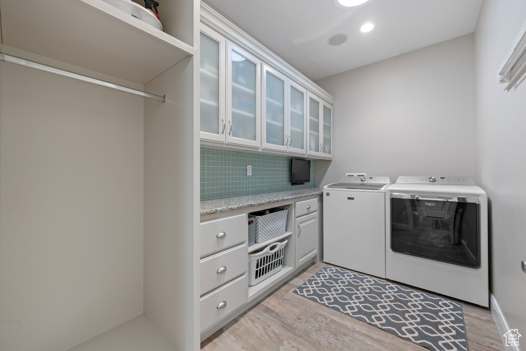 Clothes washing area with light hardwood / wood-style flooring, washing machine and dryer, and cabinets