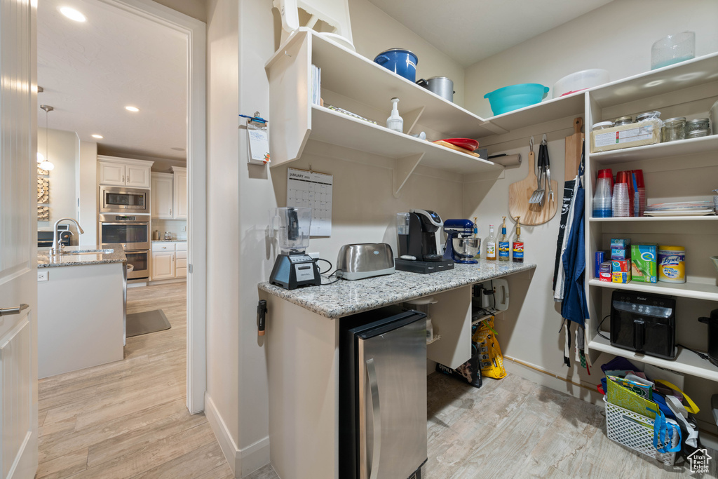 Interior space with appliances with stainless steel finishes, decorative light fixtures, wine cooler, light hardwood / wood-style floors, and light stone countertops