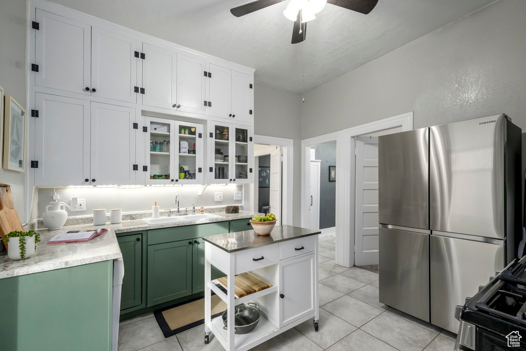 Kitchen with green cabinets, stainless steel fridge, sink, and white cabinets