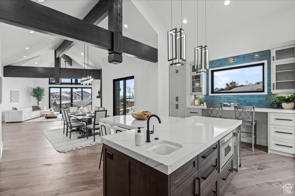 Kitchen featuring pendant lighting, white cabinetry, an island with sink, sink, and light stone countertops