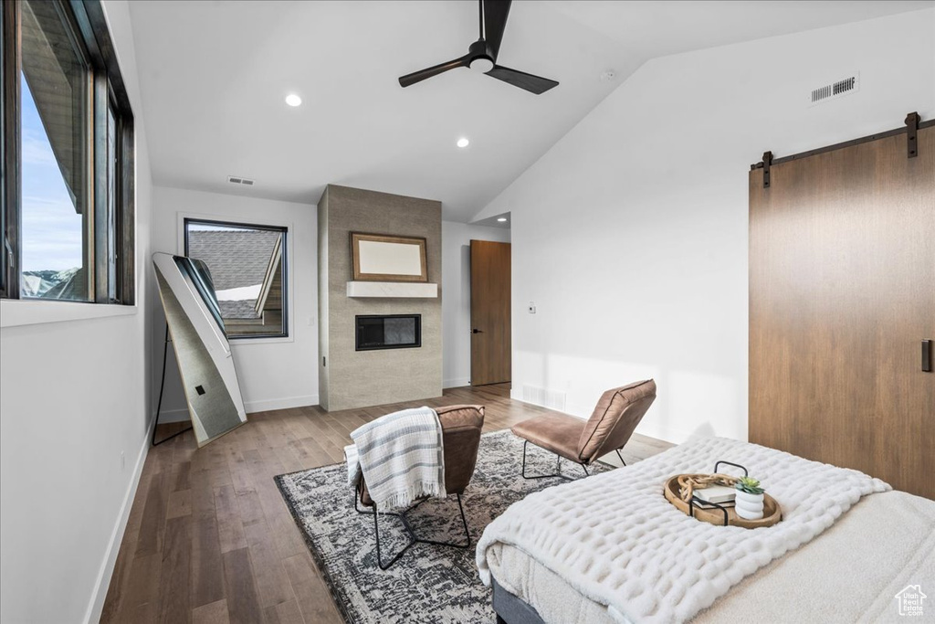 Bedroom with lofted ceiling, a large fireplace, hardwood / wood-style flooring, ceiling fan, and a barn door