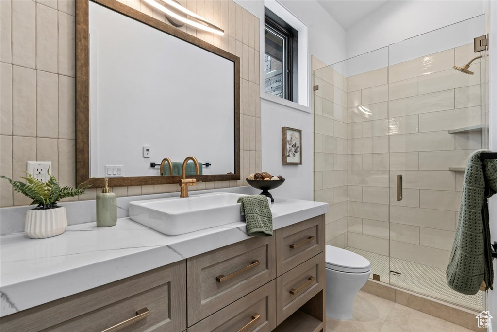 Bathroom featuring walk in shower, toilet, tile walls, vanity, and tile patterned flooring