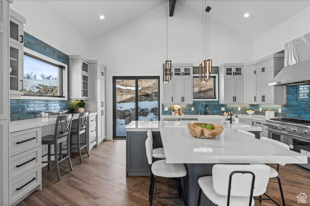 Kitchen with decorative light fixtures, dark hardwood / wood-style flooring, a kitchen breakfast bar, a large island, and wall chimney range hood