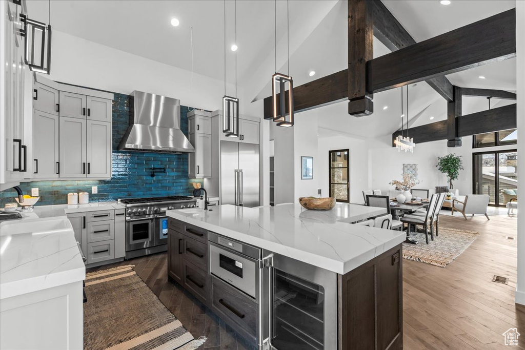 Kitchen with a kitchen island with sink, pendant lighting, high quality appliances, and wall chimney exhaust hood