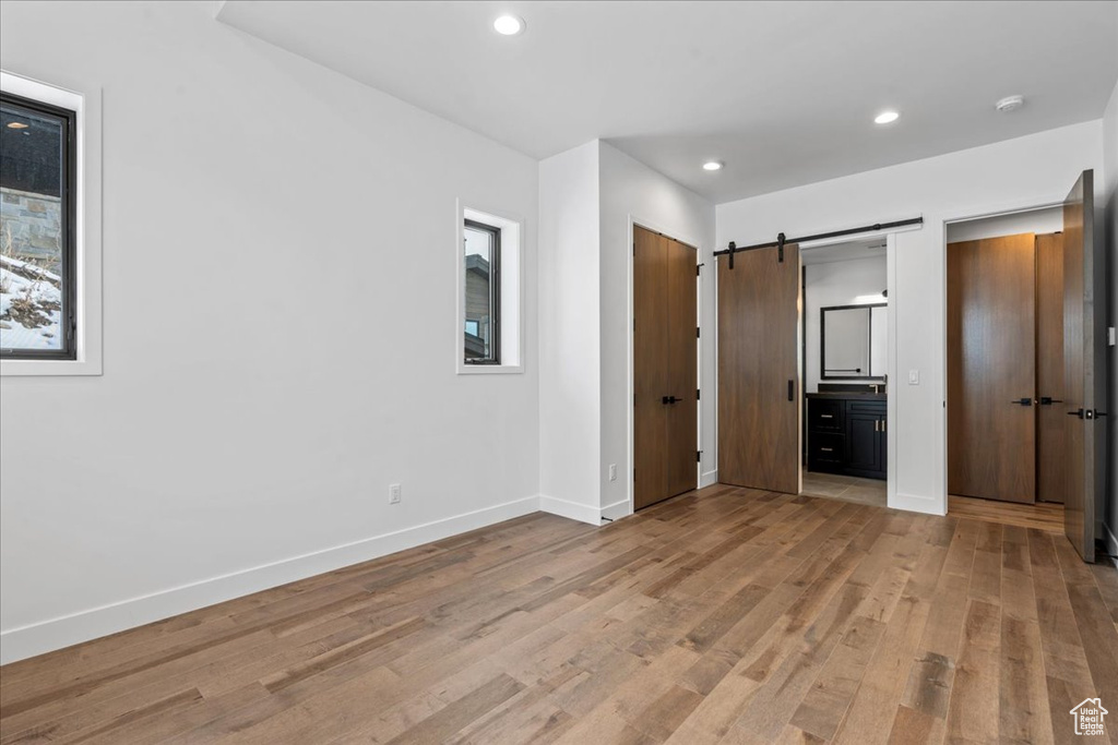 Unfurnished bedroom featuring connected bathroom, a barn door, and light hardwood / wood-style floors