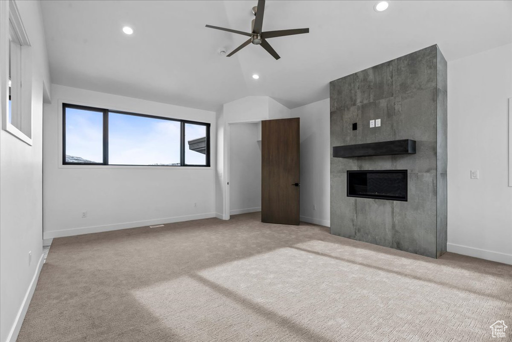 Unfurnished living room with ceiling fan, light colored carpet, lofted ceiling, and a fireplace