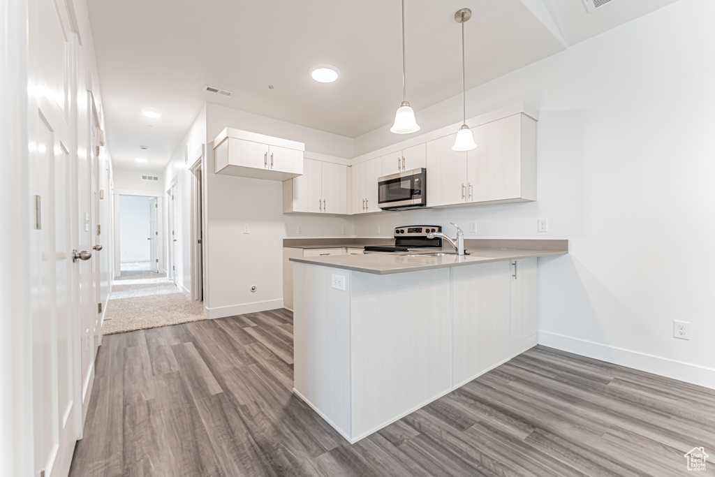 Kitchen with stainless steel microwave, range with electric stovetop, a peninsula, wood finished floors, and white cabinetry