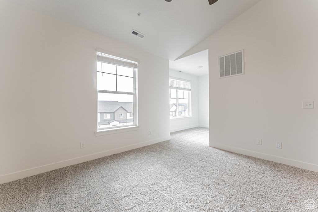 Empty room with light carpet, ceiling fan, and vaulted ceiling