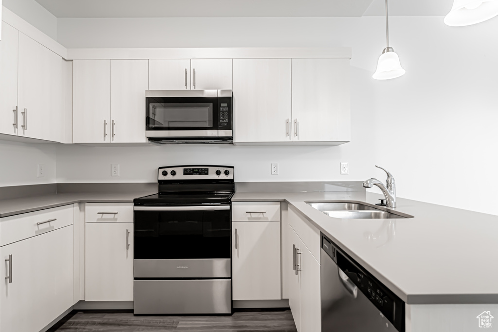 Kitchen featuring appliances with stainless steel finishes, a peninsula, dark wood-style floors, and white cabinets
