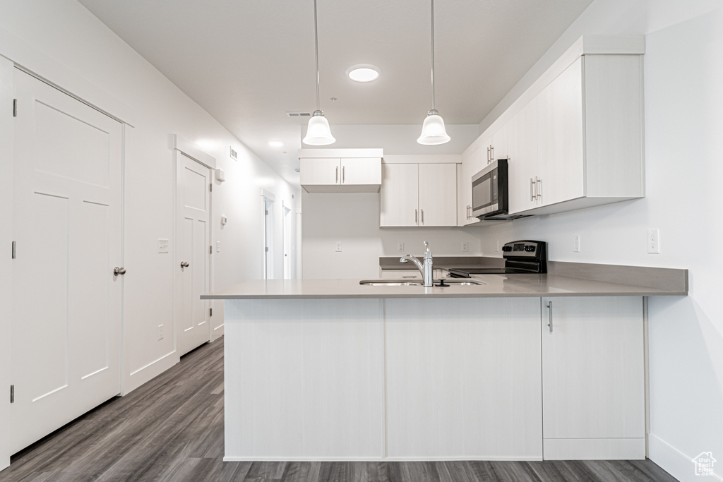Kitchen featuring stainless steel appliances, a peninsula, dark wood-type flooring, white cabinets, and pendant lighting