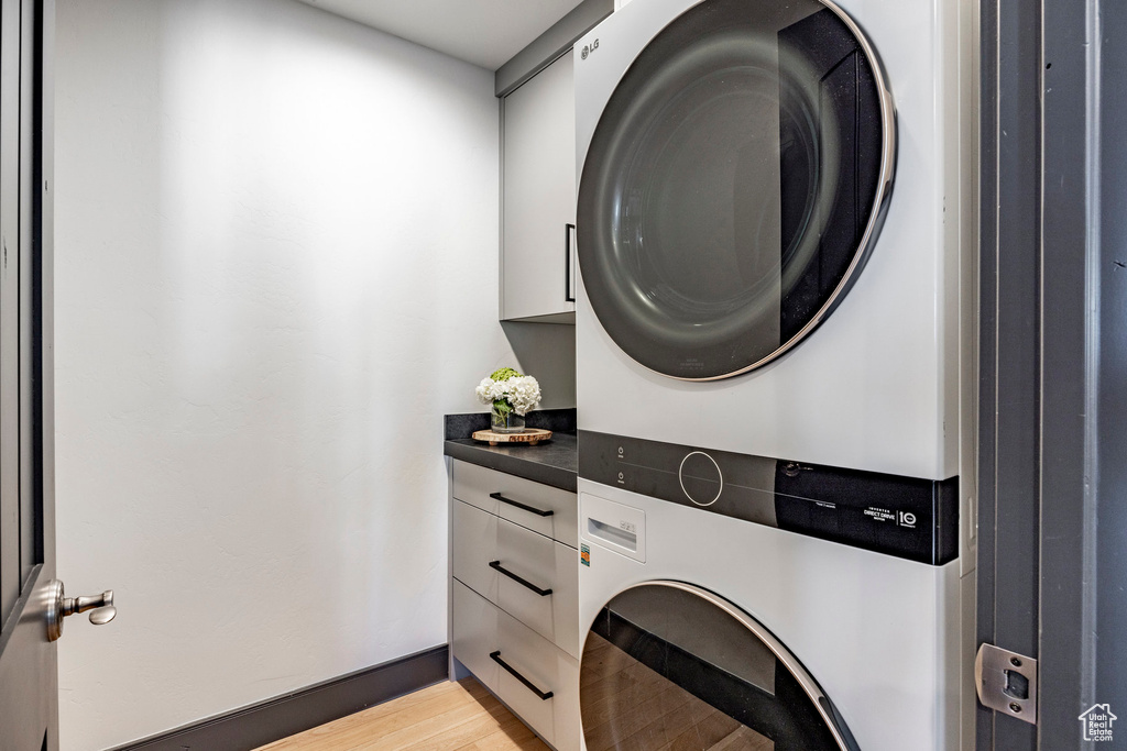 Clothes washing area featuring stacked washing machine and dryer, cabinet space, and light wood-style floors