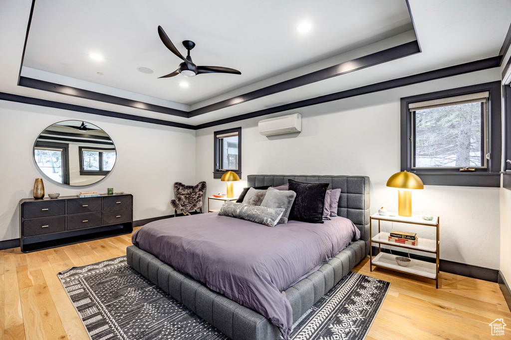 Bedroom with a raised ceiling, a wall mounted AC, multiple windows, light wood-style floors, and recessed lighting