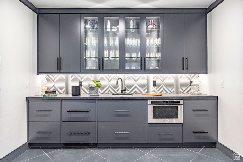 Bar area featuring a sink, dark tile patterned floors, tasteful backsplash, and stainless steel oven