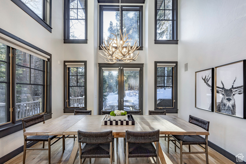 Dining area featuring a chandelier, plenty of natural light, wood finished floors, a towering ceiling, and french doors