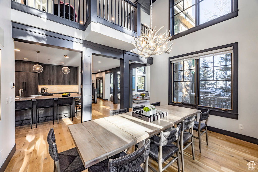 Dining area featuring light wood-style floors, baseboards, a chandelier, and a towering ceiling