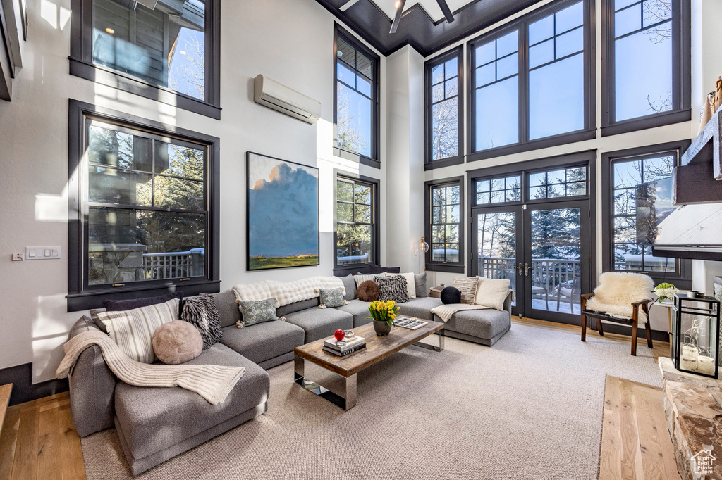 Living area with a wall mounted AC, a high ceiling, and wood finished floors