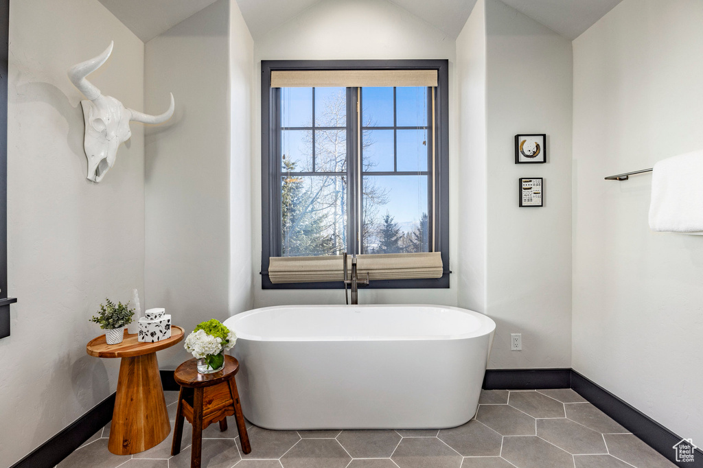 Bathroom featuring a freestanding tub, baseboards, tile patterned floors, and lofted ceiling
