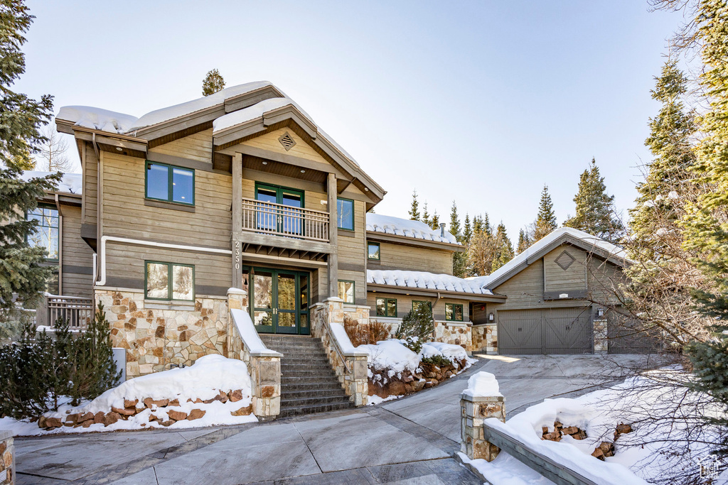 Craftsman house featuring a balcony, stone siding, a garage, french doors, and concrete driveway