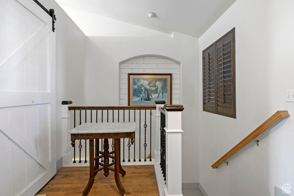 Corridor with light hardwood / wood-style flooring, vaulted ceiling, and a barn door