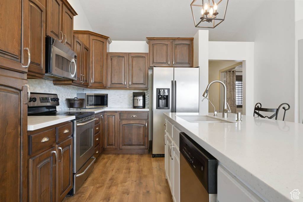Kitchen with sink, tasteful backsplash, pendant lighting, stainless steel appliances, and light hardwood / wood-style floors