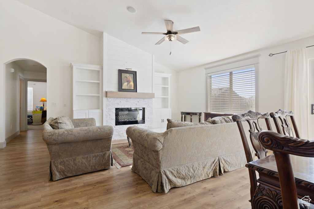 Living room featuring vaulted ceiling, a stone fireplace, ceiling fan, light hardwood / wood-style floors, and built in shelves
