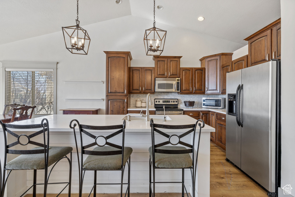 Kitchen with vaulted ceiling, appliances with stainless steel finishes, a kitchen island with sink, and backsplash