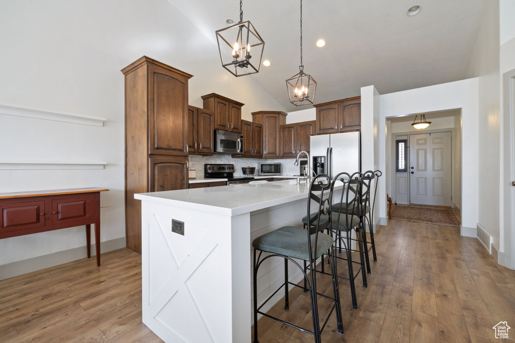 Kitchen with a large island, lofted ceiling, hanging light fixtures, stainless steel appliances, and a kitchen bar