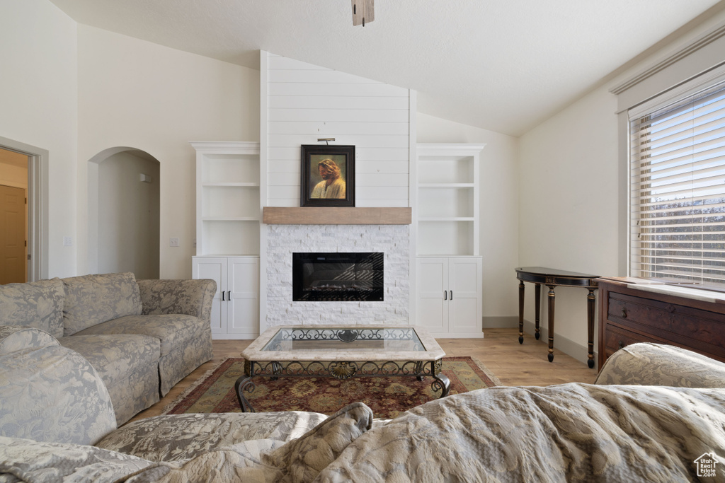Living room with vaulted ceiling, built in features, a fireplace, and light wood-type flooring